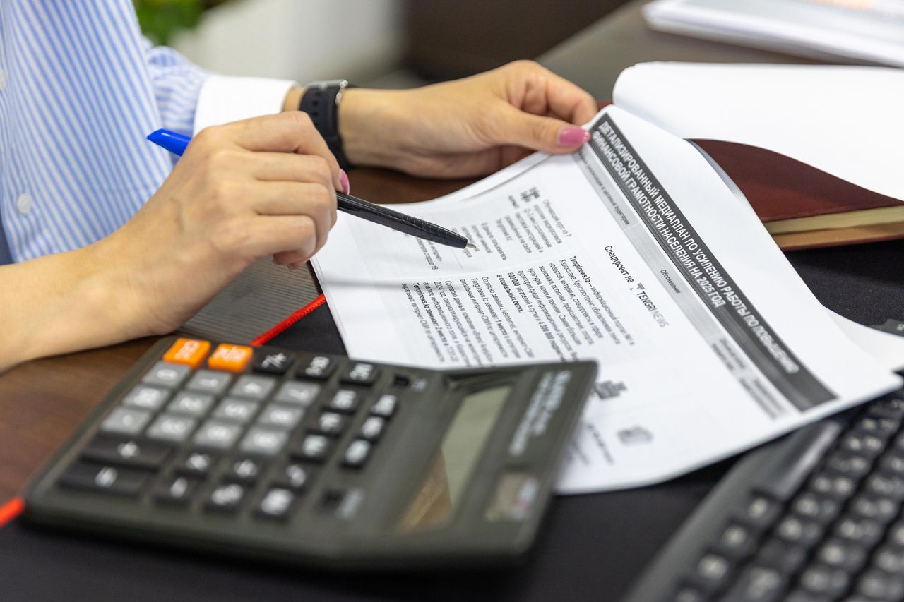 services-02 Close-up of a person analyzing financial documents using a calculator and pen.
