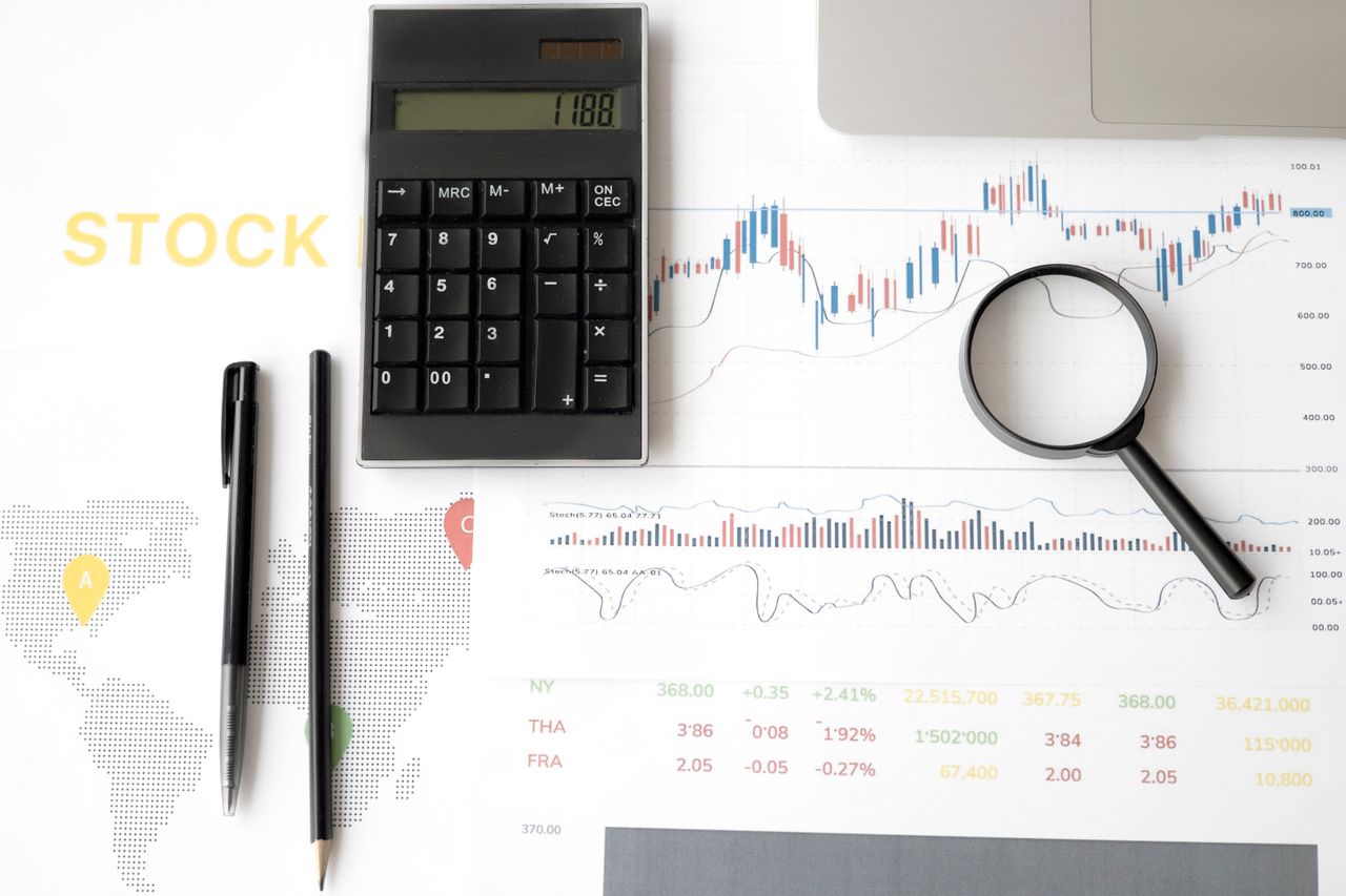 hero-img-01 Flat lay of stock market analysis tools including calculator, graphs, and magnifying glass.