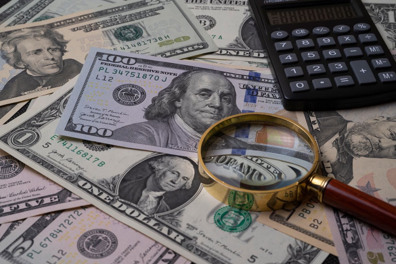 about-01 US currency bills with magnifying glass and calculator, symbolizing financial analysis.